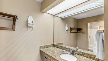 A bathroom with a granite countertop sink, a mirror, a towel rack, and a shower visible through the glass door.