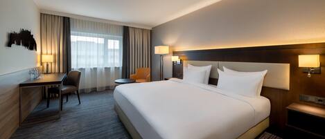 Ein Hotelzimmer mit einem großen Bett, einem Schreibtisch, einem Stuhl und einem fenster mit Vorhängen.