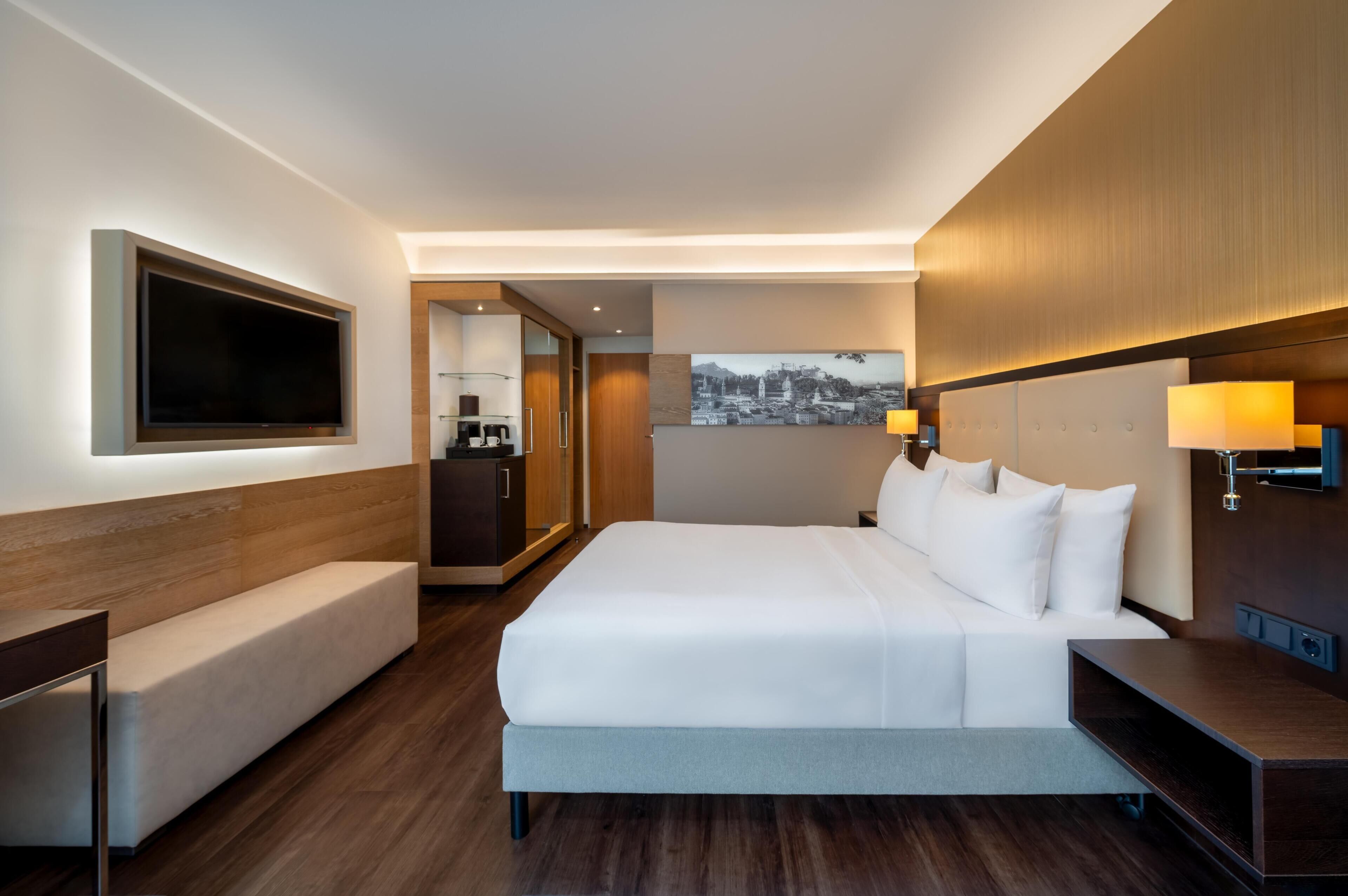 A hotel room with a large bed, a flat-screen TV, a desk, and a painting on the wall.