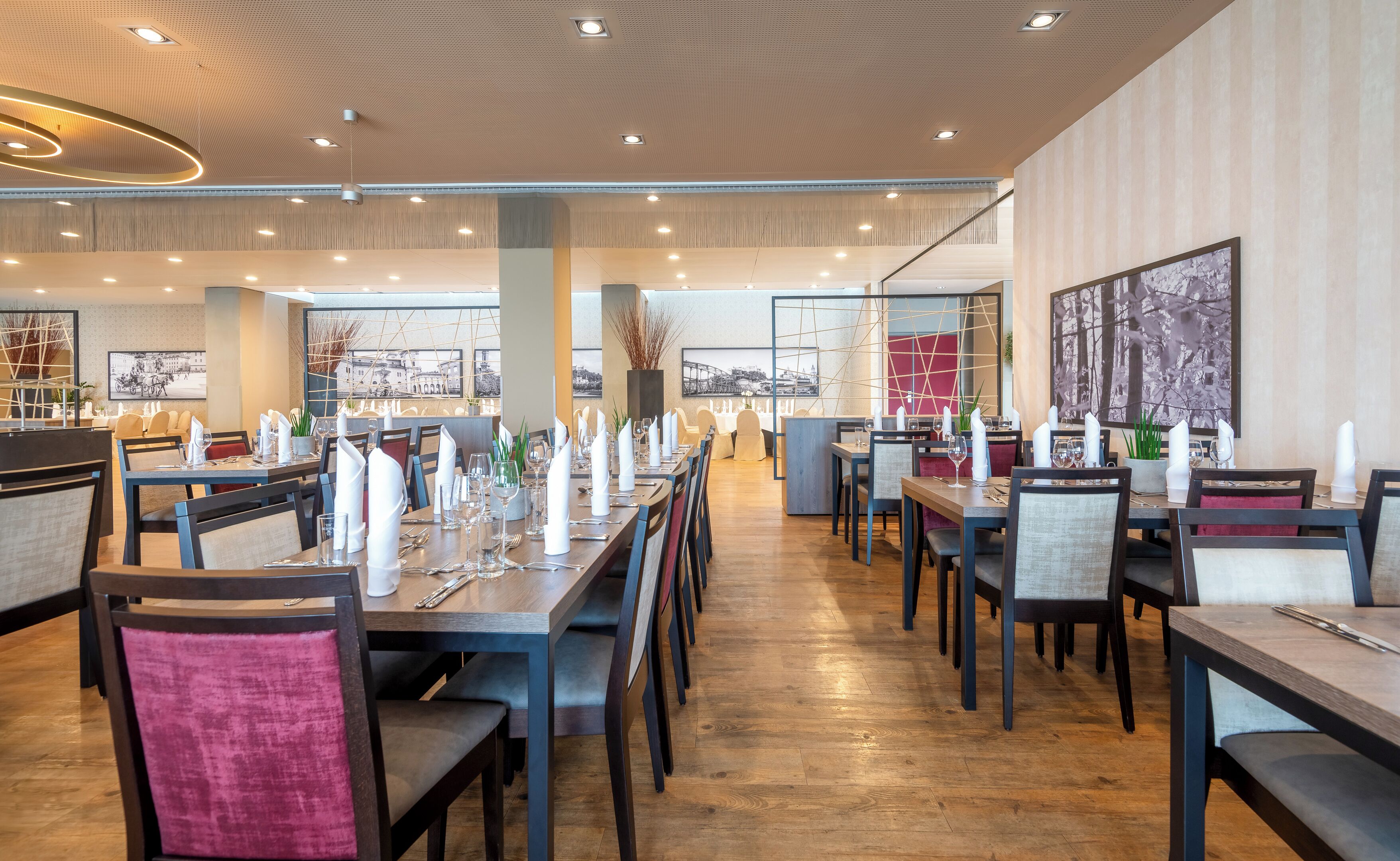 Un restaurant moderne avec des tables et des chaises en bois, de grandes fenêtres et des œuvres d’art accrochées aux murs.