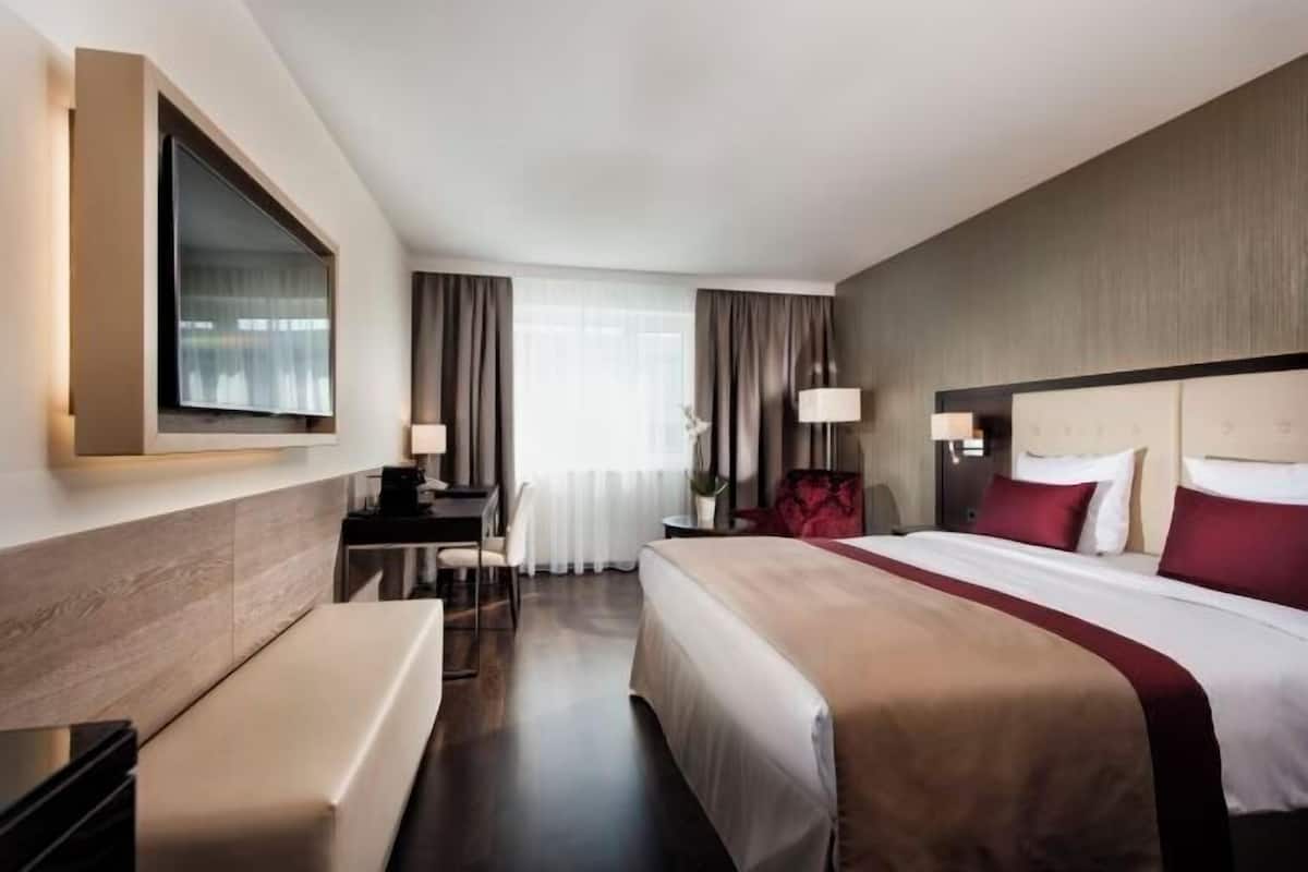 Une chambre dâhĂŽtel avec un grand lit, un bureau, une chaise, une tĂ©lĂ©vision et une fenĂȘtre avec des rideaux.