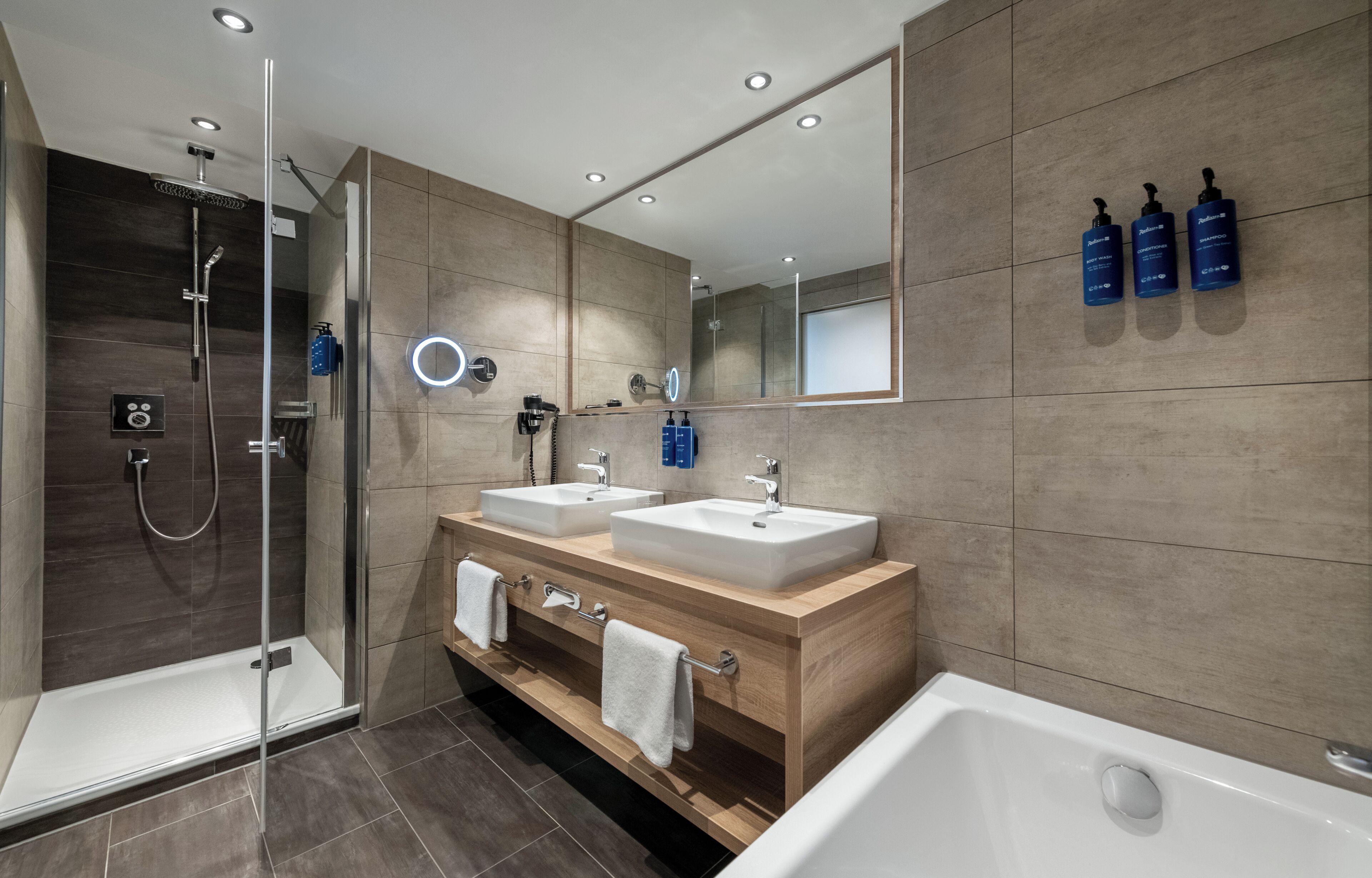A modern bathroom with a glass-enclosed shower, two sinks, a large mirror, and toiletries on the wall.