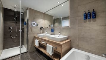 A modern bathroom with a glass-enclosed shower, two sinks, a large mirror, and toiletries on the wall.