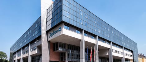 Un hotel Radisson Blu con fachada de vidrio moderno, múltiples accesos y cielo despejado.