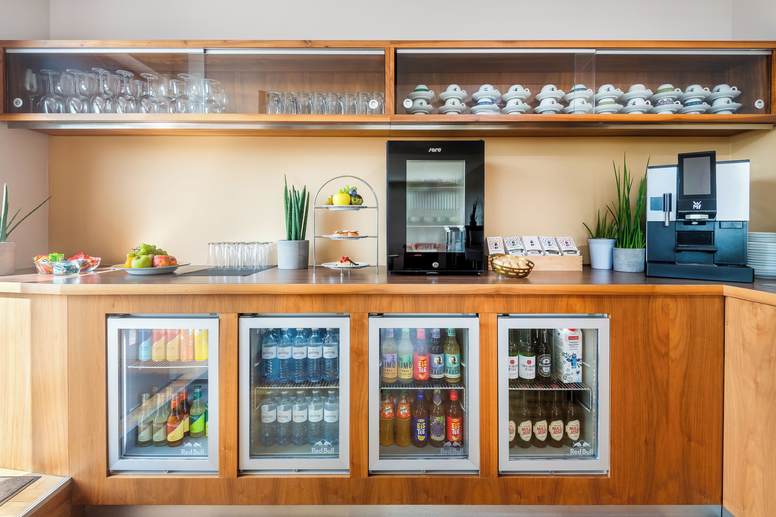 A bar area with a refrigerator stocked with beverages, a coffee machine, and a display of glassware.