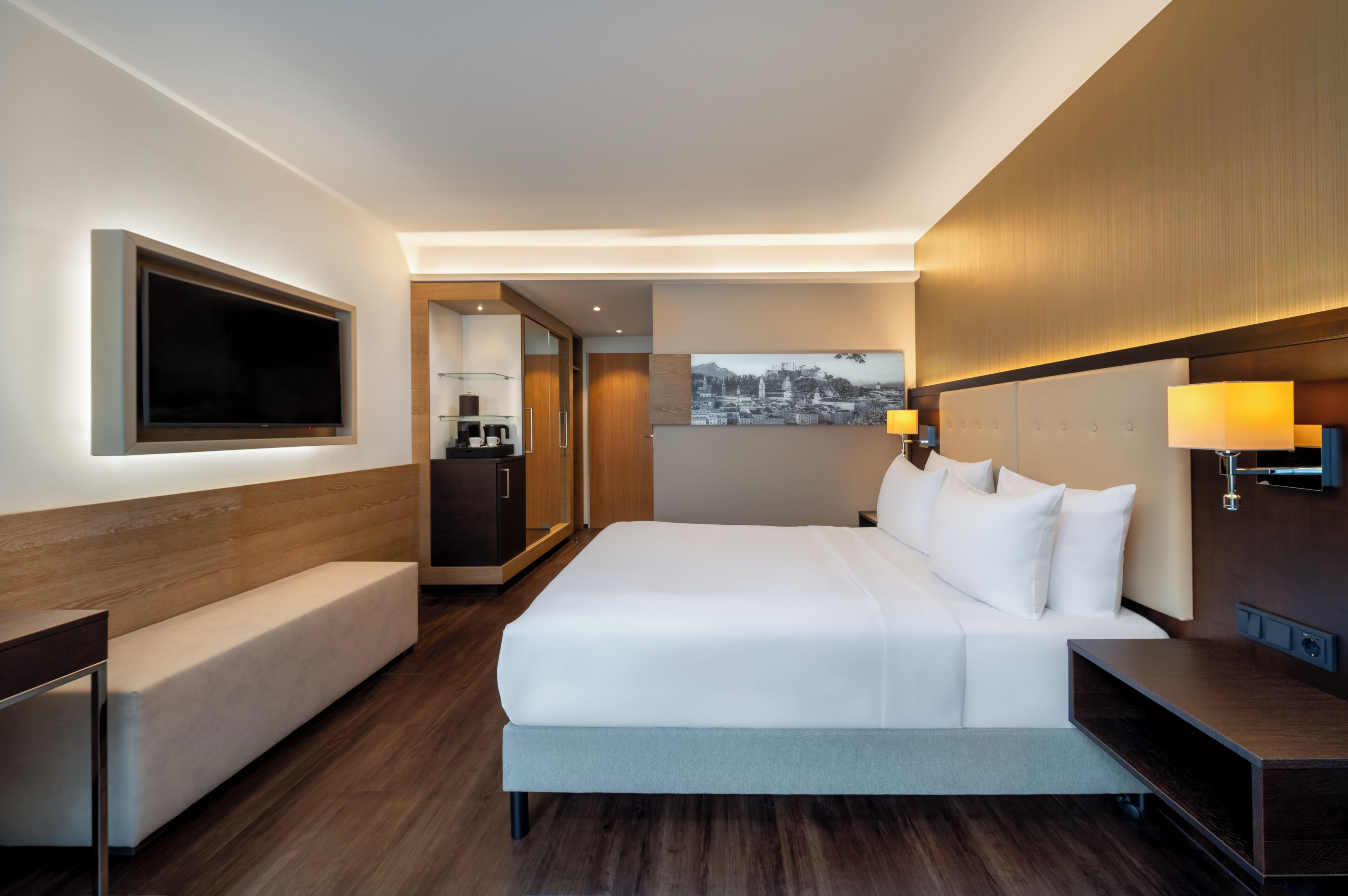 A hotel room with a large bed, a TV, a desk, and a painting on the wall.