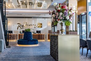 A hotel reception area with a blue seating area, a large floral arrangement, and a reception desk with a TV. - Radisson Blu Hotel & Conference Centre, Salzburg (Salzburg)