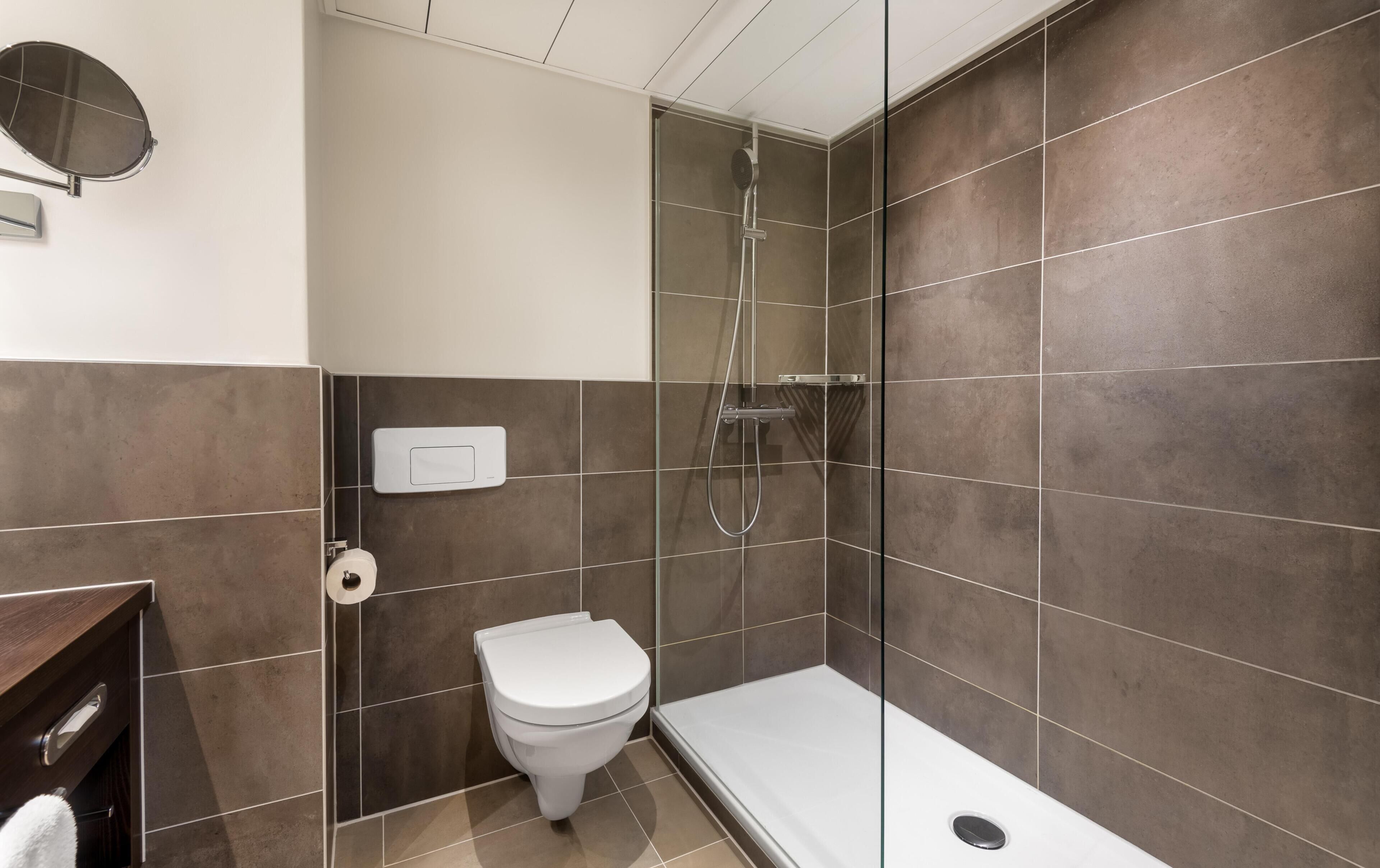A modern bathroom with a toilet, a shower, and a glass-enclosed shower area.