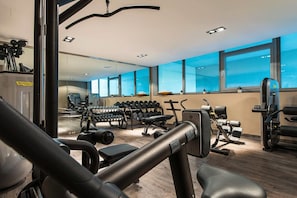 Un gimnasio con equipo de ejercicio, un espejo grande y amplias ventanas.