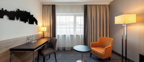 Habitación de hotel con escritorio, silla, cama y un cuadro de arte urbano en la pared.