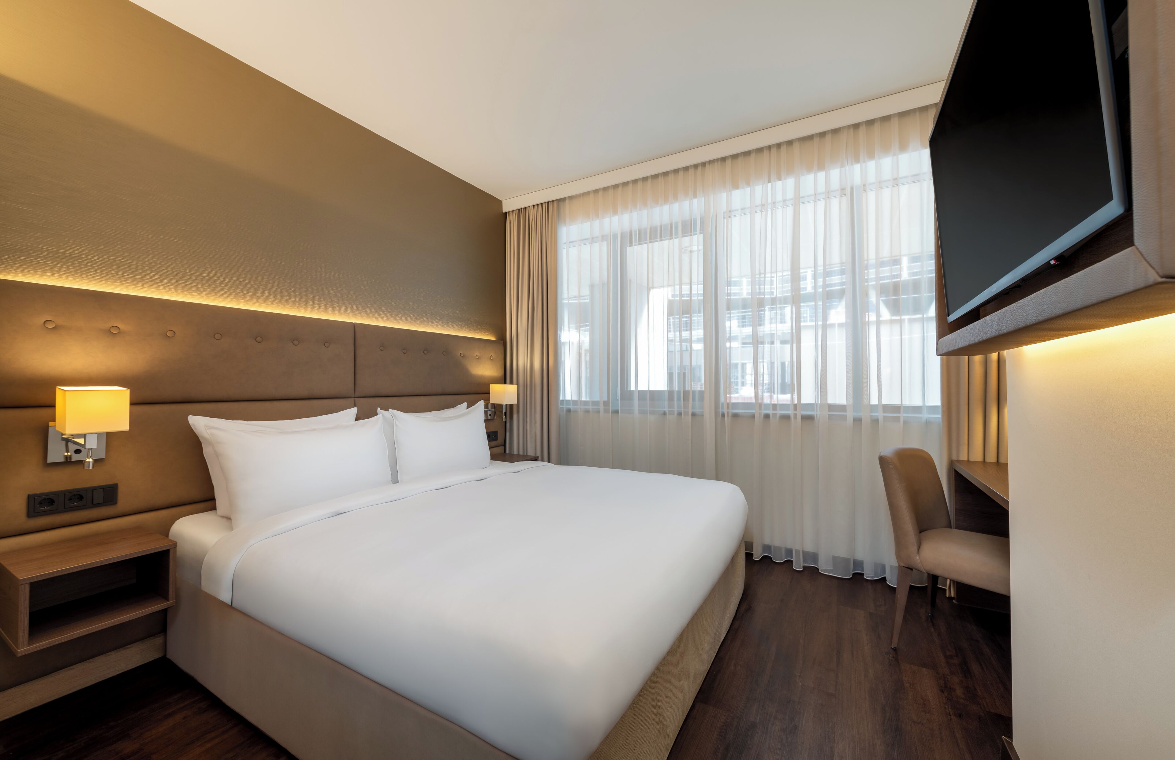 Habitación de hotel con una cama grande, televisión montada en la pared, mesita de noche y una silla.