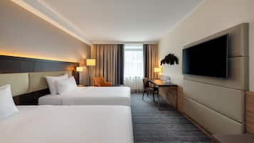 Une chambre d’hôtel avec deux lits, un bureau, une chaise, un téléviseur à écran plat et une fenêtre avec des rideaux.
