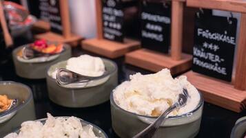 Un bufé con diversos alimentos, incluyendo un tazón de queso fresco, un tazón de arroz y un tazón de ensalada. También hay carteles que indican las diferentes secciones del bufé.
