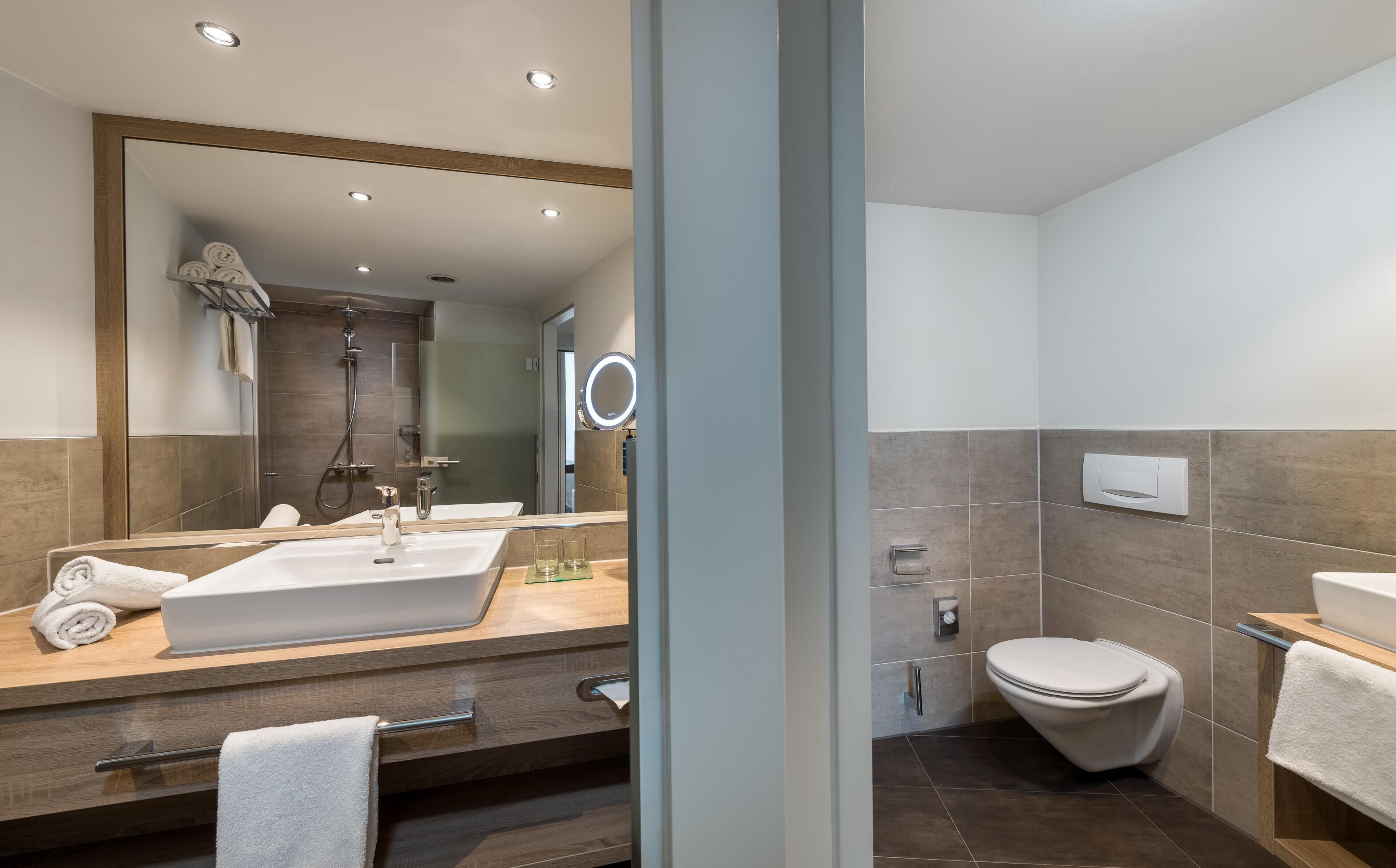 A modern bathroom with a large mirror, a sink, a toilet, and a shower.