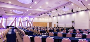 A conference room with rows of tables and chairs, a stage, and a large screen. - Radisson Blu Hotel & Conference Centre, Salzburg (Salzburg)