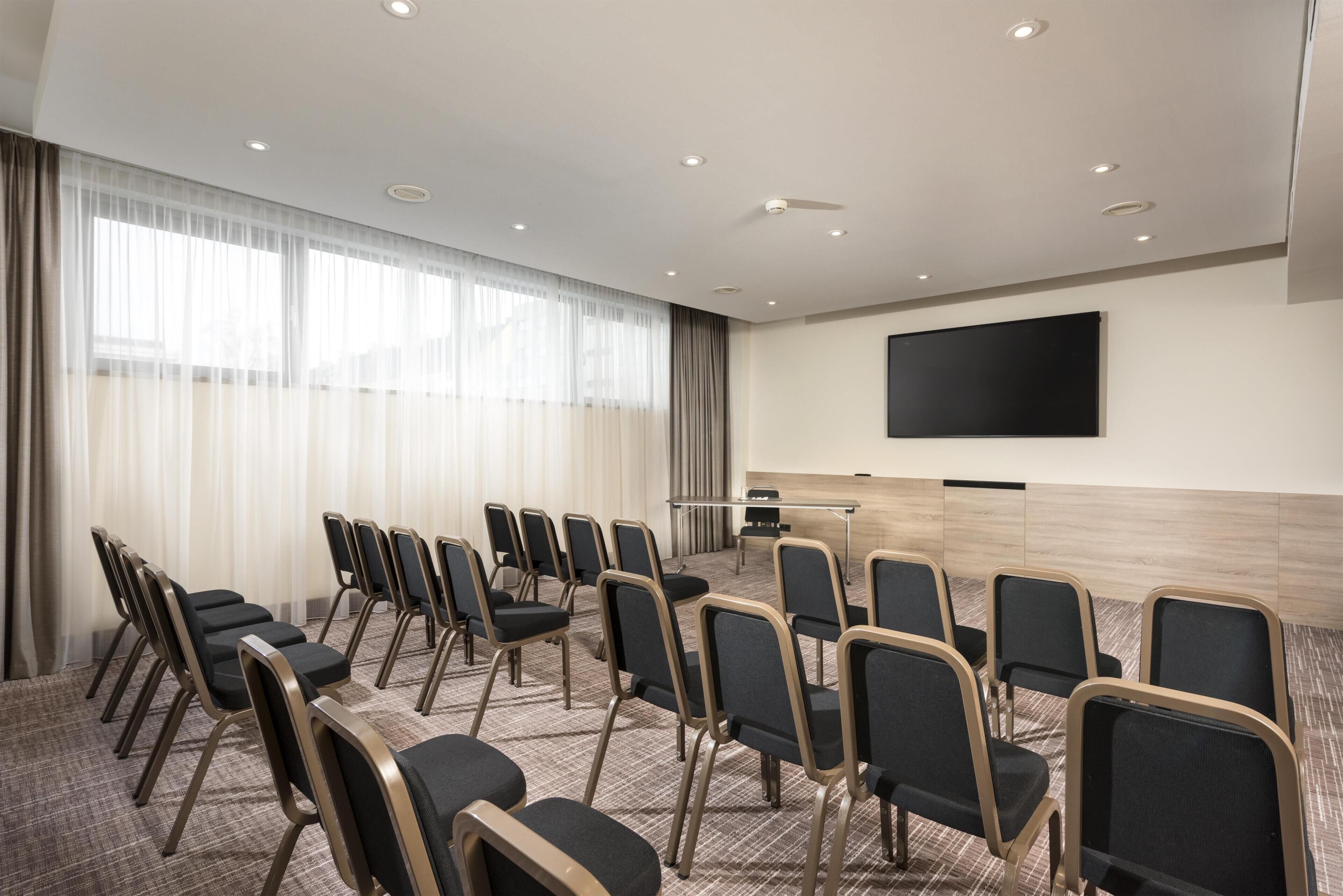 A conference room with rows of chairs, a large flat-screen TV, and a podium.