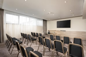 A conference room with rows of chairs, a large flat-screen TV, and a podium. - Radisson Blu Hotel & Conference Centre, Salzburg (Salzburg)