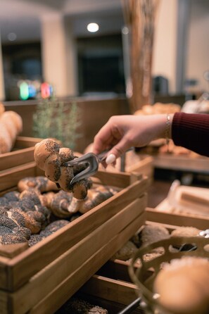 A hand using tongs to handle poppy-seeded bread in a wooden bread display.