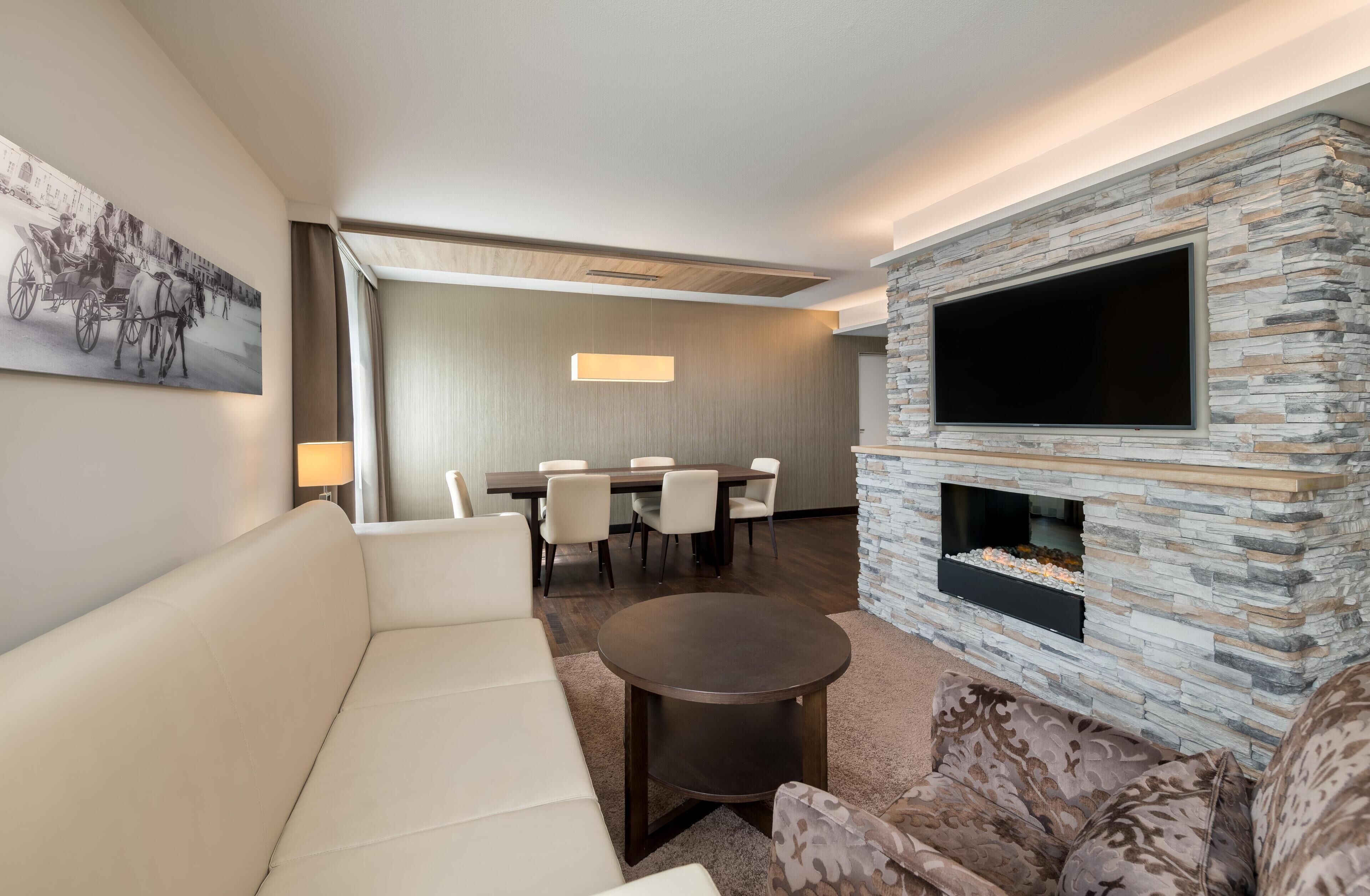 Ein Hotelzimmer mit einer Couch, einem Esstisch mit Stühlen, einem Flachbildfernseher an einer Steinwand und einem Kamin.