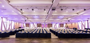 Un amplio salón de conferencias con filas de mesas y sillas, equipado con iluminación y sistemas de proyección.