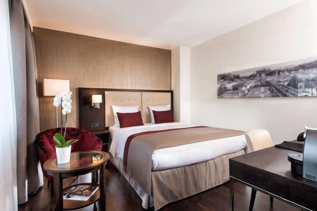 Ein Hotelzimmer mit Bett, Schreibtisch, Stuhl, Lampe und einem Bild an der Wand.