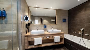A modern bathroom with two sinks, a bathtub, a mirror with a built-in light, and a phone.
