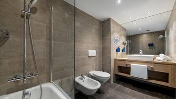 Un baño moderno con ducha envuelta en vidrio, una bañera independiente, un bidé y un tocador de madera con espejo y perchero.