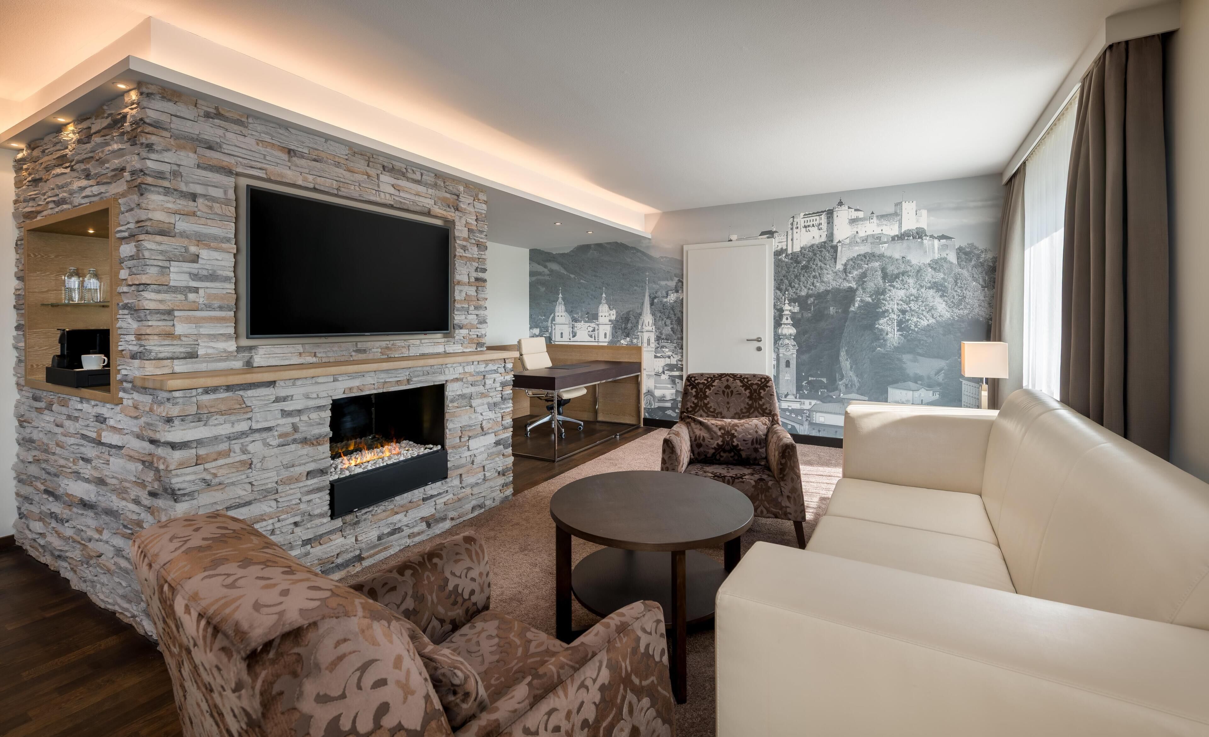 A modern living room with a stone fireplace, a flat-screen TV, a sofa, a coffee table, and a view of a castle through a window.