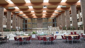 A spacious indoor area with multiple tables and chairs, high ceilings with skylights, and brick walls. - Clarion Hotel & Conference Center Lansing West (Lansing)
