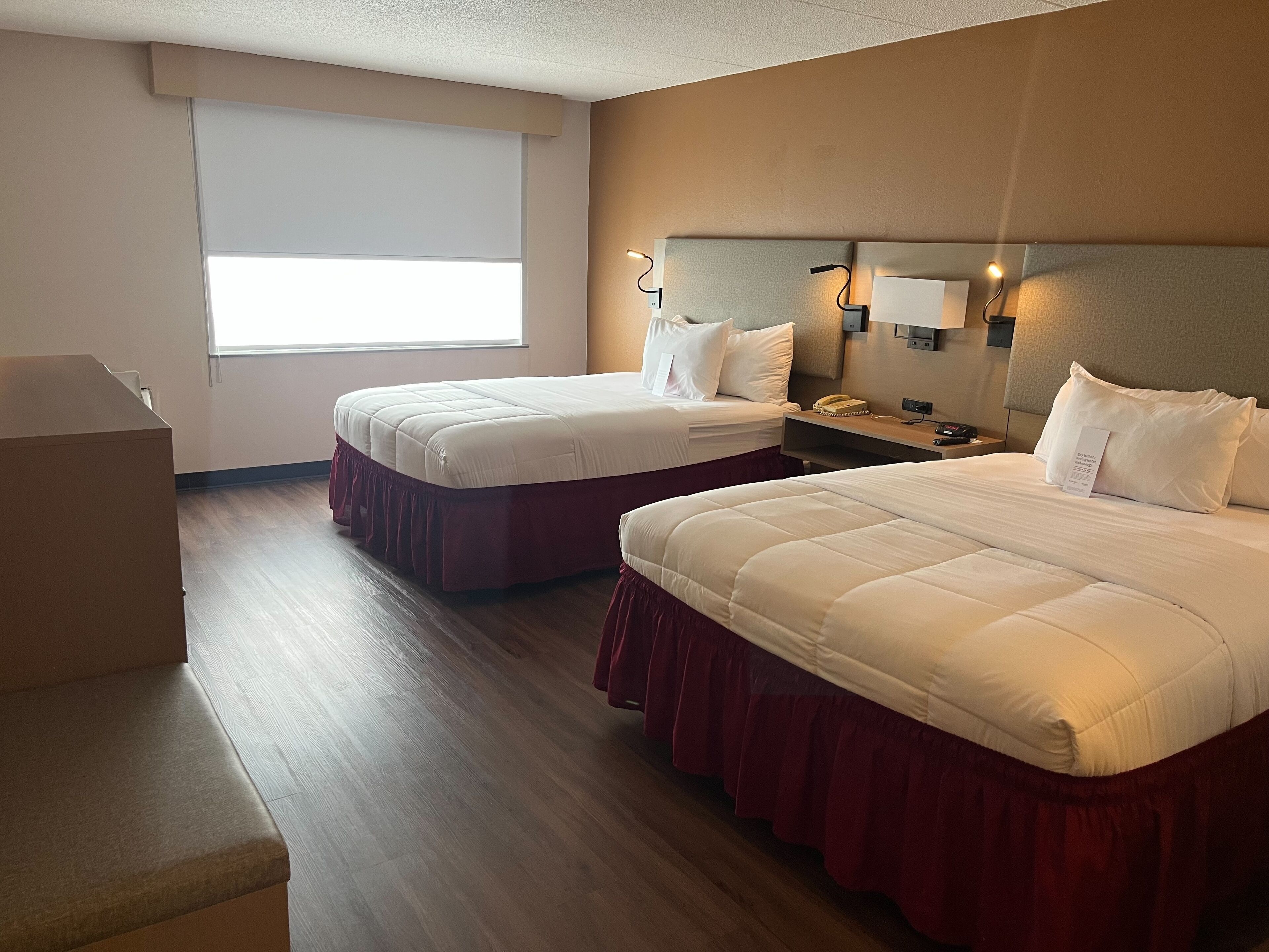 A hotel room with two beds, a desk, and a window.