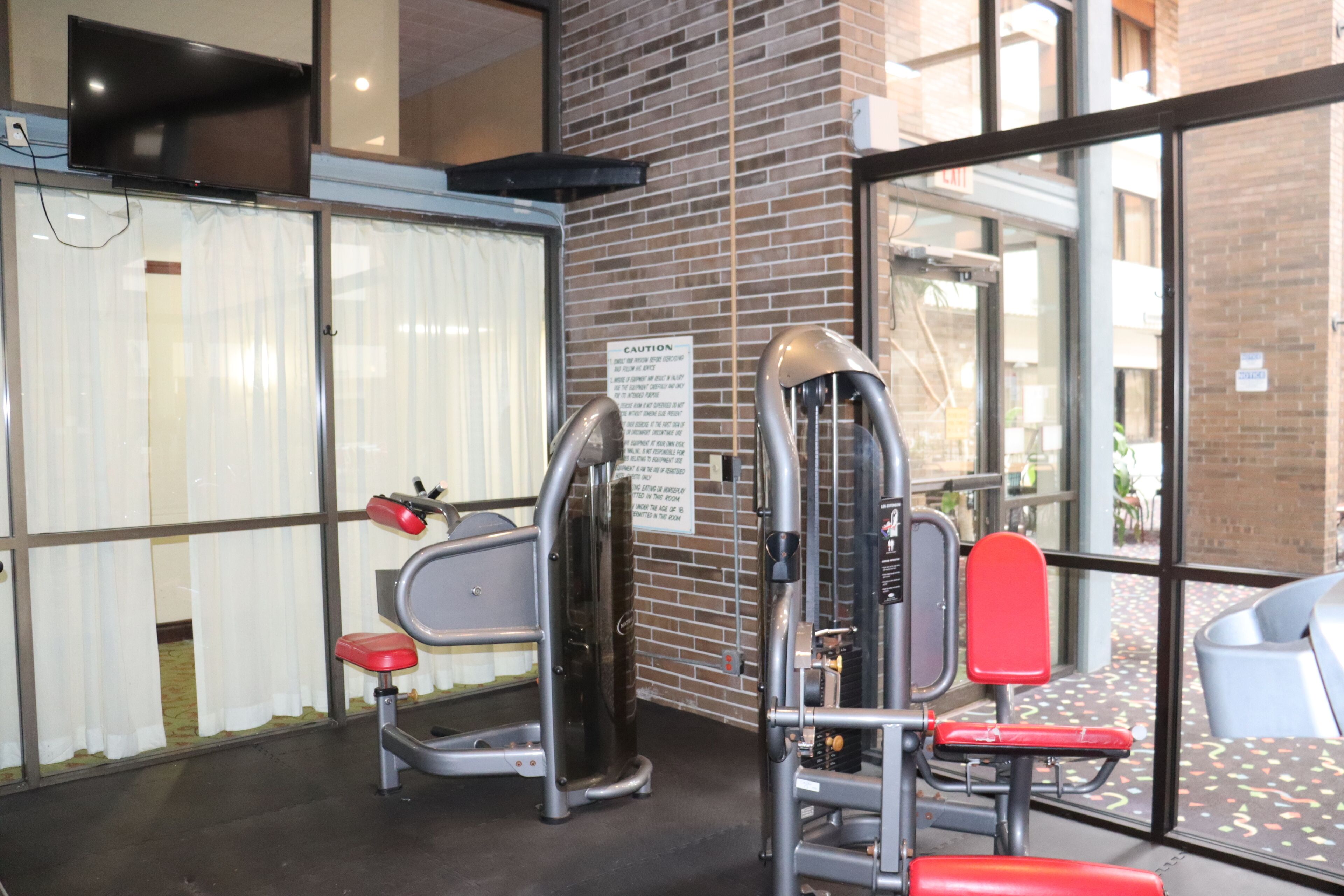 A gym with exercise equipment, a caution sign, and a view of the outside through large windows.