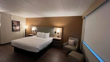 Una habitación de hotel con una cama grande, mesitas de noche, una silla y un televisor de pantalla plana.