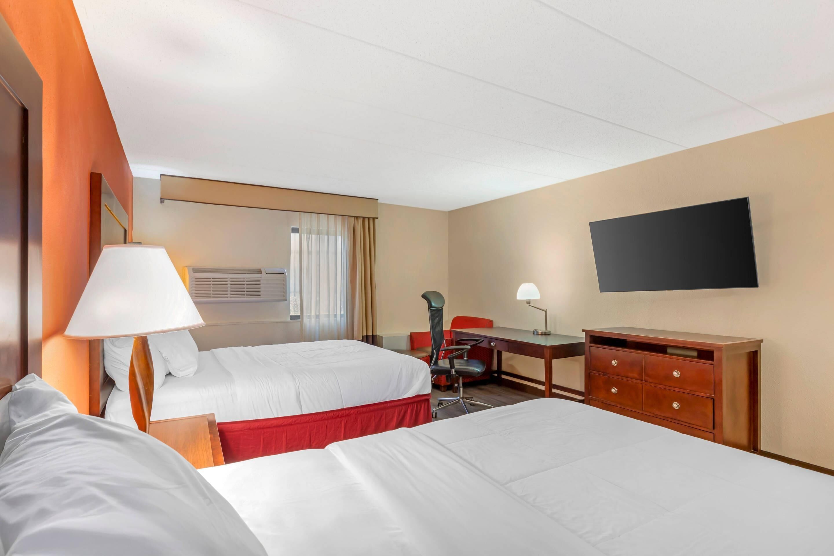 A hotel room with two beds, a desk, a chair, a TV, and a dresser.