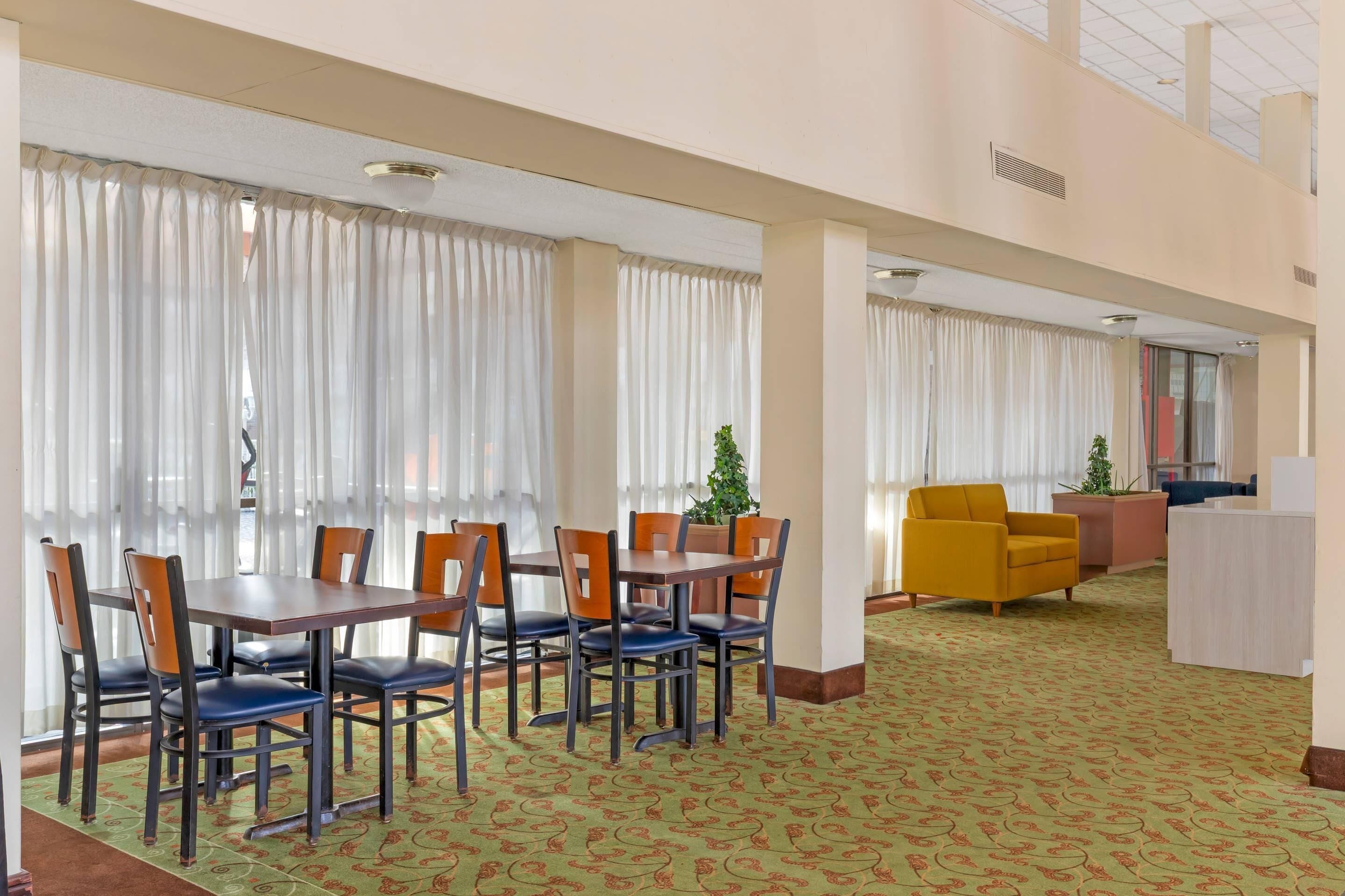 A hotel lobby with a dining area featuring a table and chairs, a reception desk, and a patterned carpet.