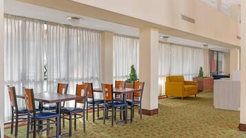 A hotel lobby with a dining area featuring a table and chairs, a reception desk, and a patterned carpet.