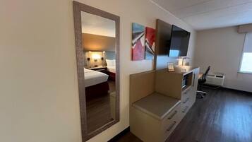 Une chambre d’hôtel comprenant un lit, une table de chevet, une lampe, une œuvre d’art, une télévision et un petit coin salon.