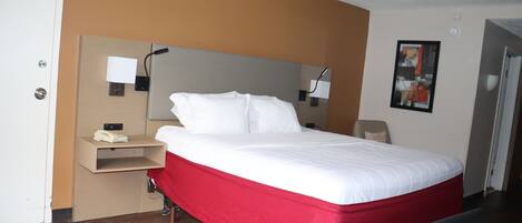 A hotel room with a bed, a desk with a phone, and a wall-mounted lamp.