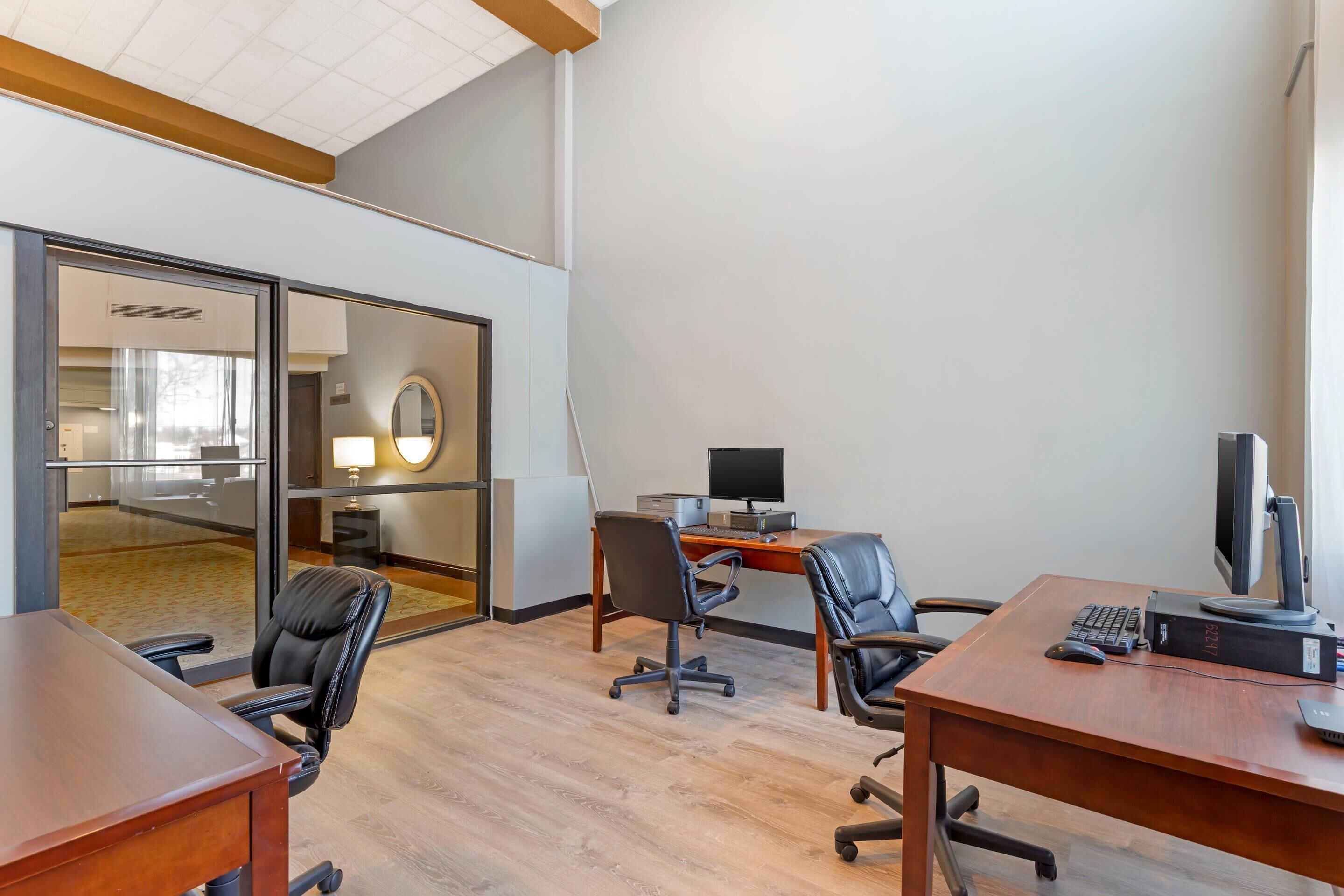 A modern office space with glass walls, wooden desks, and black office chairs.