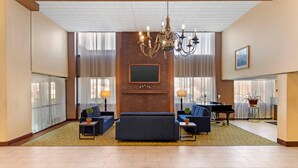A spacious living room with a large sofa, two armchairs, a piano, and a chandelier. - Clarion Hotel & Conference Center Lansing West (Lansing)