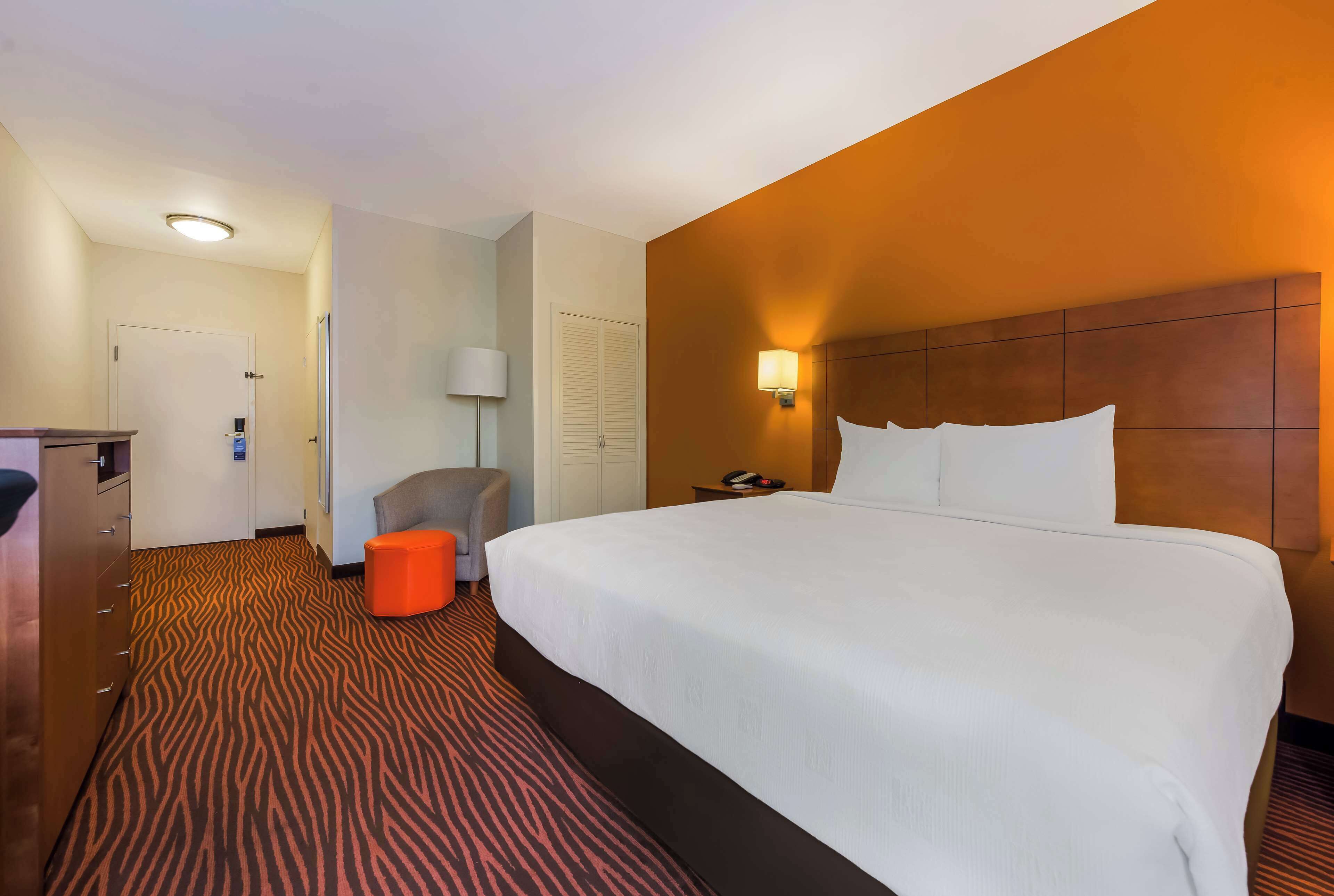 Een hotelkamer met een groot bed, een bureau, een stoel en een klein oranje poef.
