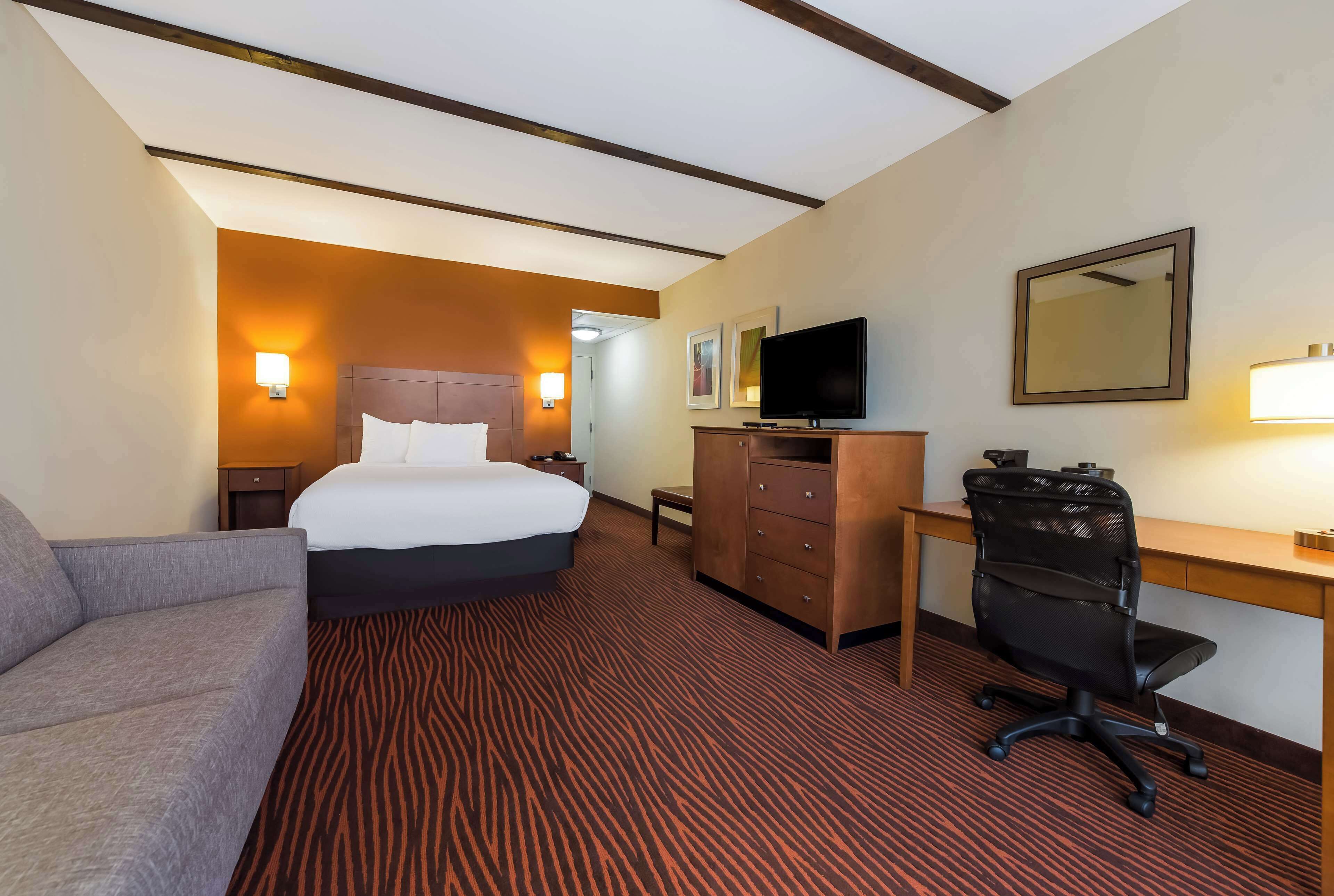 A hotel room with a bed, a desk, a chair, a television, and a mirror.