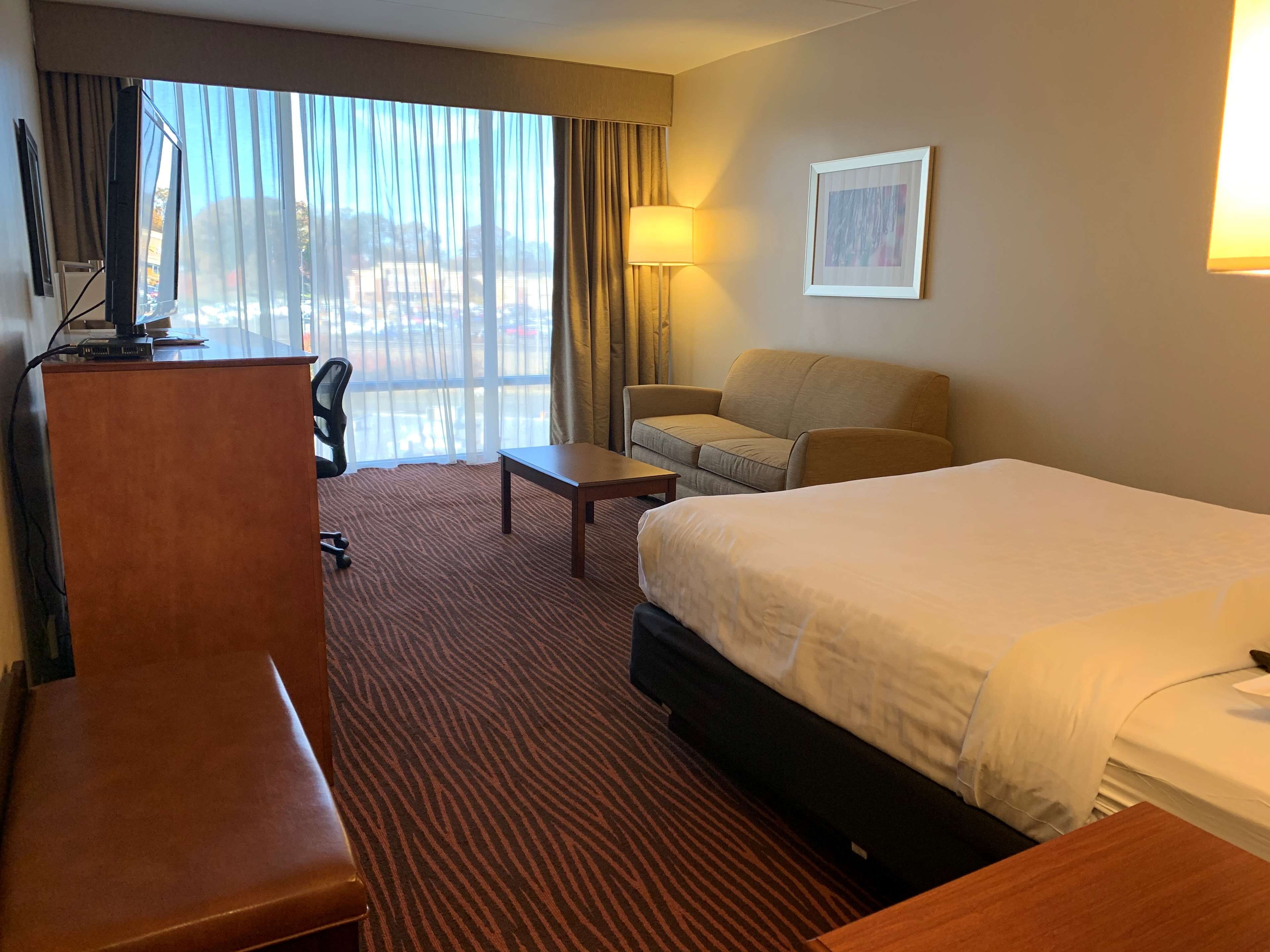 Una habitación de hotel con cama, escritorio, silla, sofá y un ventanal con cortinas.