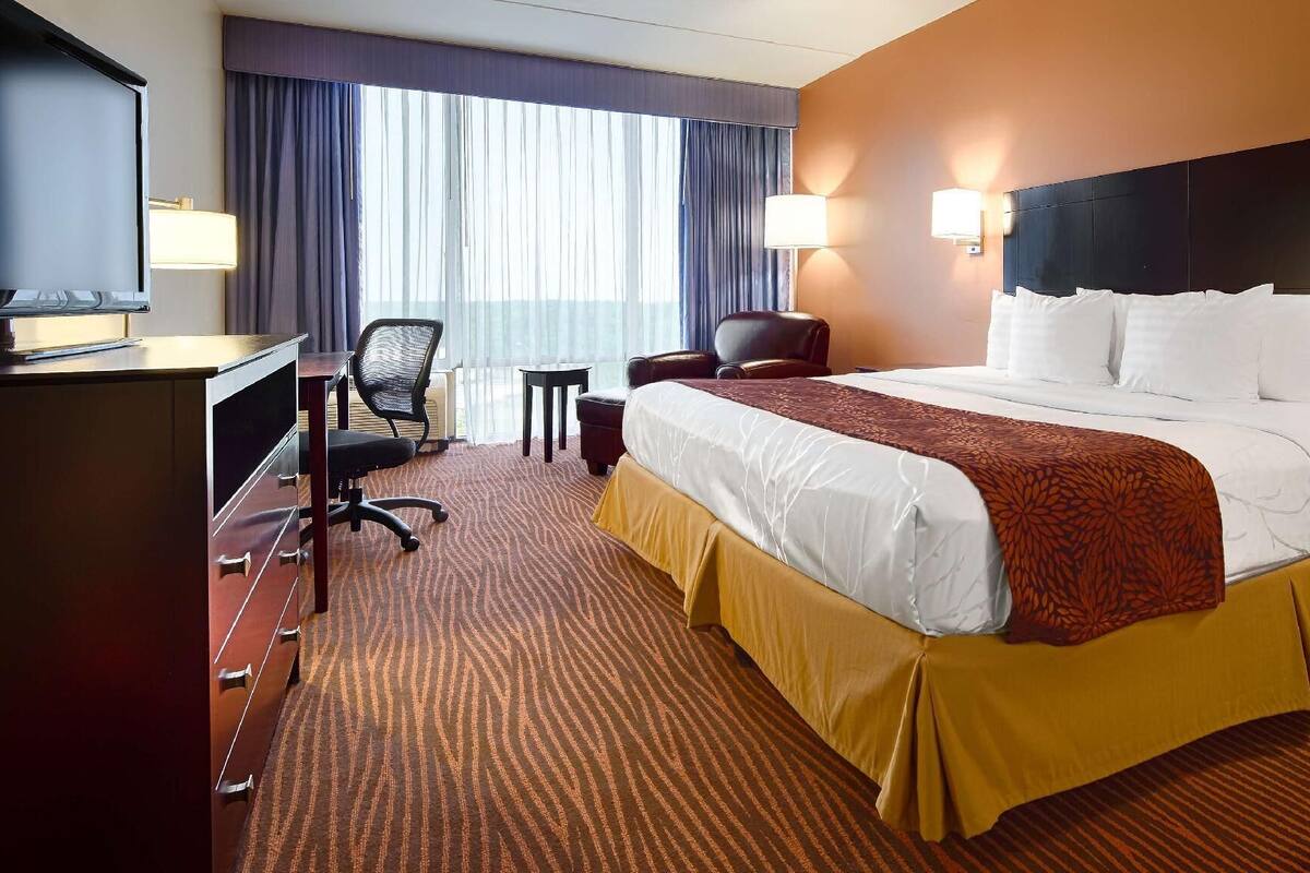 A hotel room with a large bed, a desk, a chair, a lamp, and a view of the outdoors.