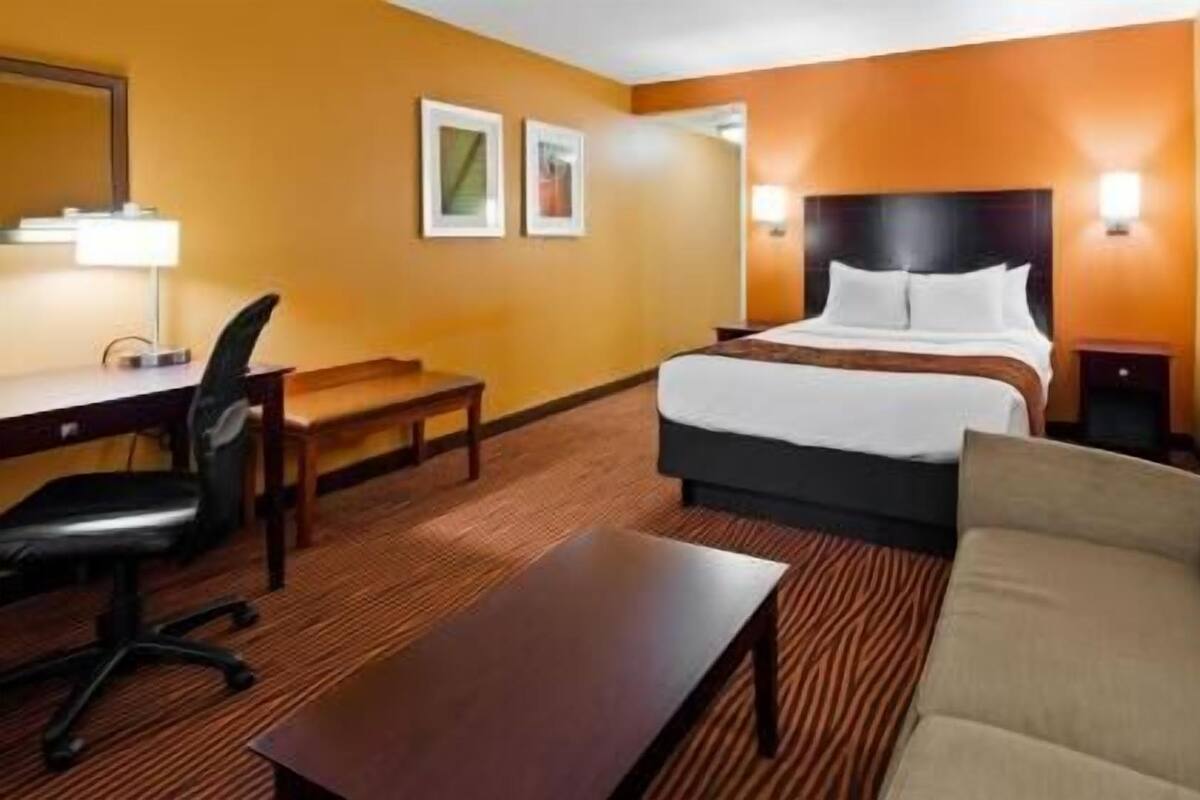 A hotel room with a bed, a desk, a chair, a sofa, and two wall-mounted lamps.