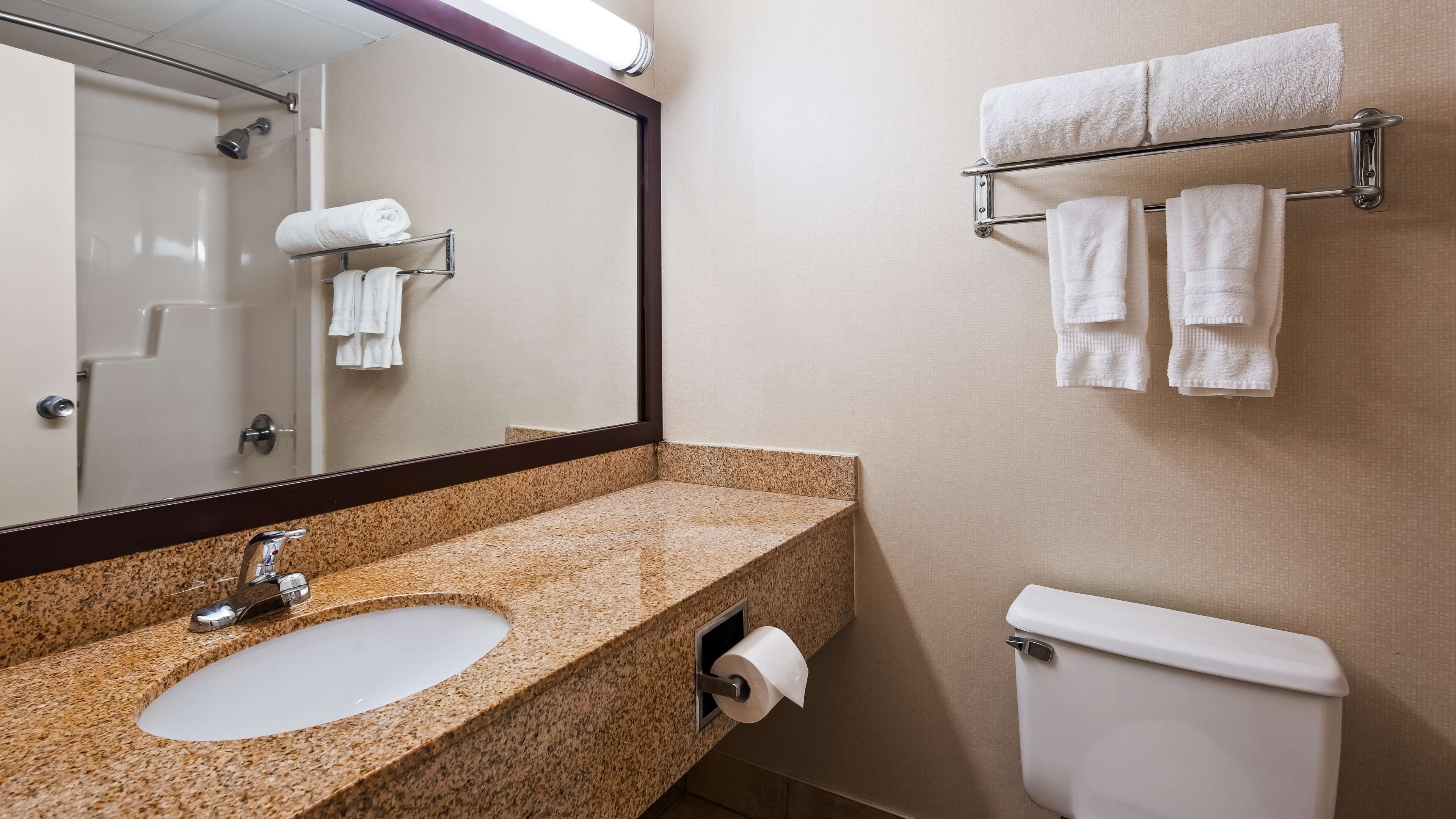 A bathroom with a granite countertop sink, a mirror, a towel rack with towels, and a toilet.