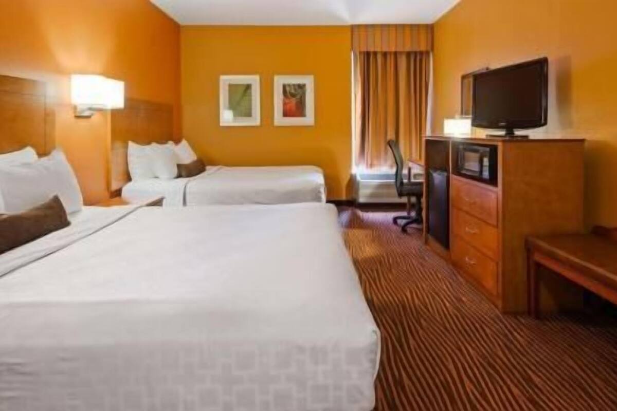 A hotel room with two beds, a desk, a television, and two framed pictures on the wall.