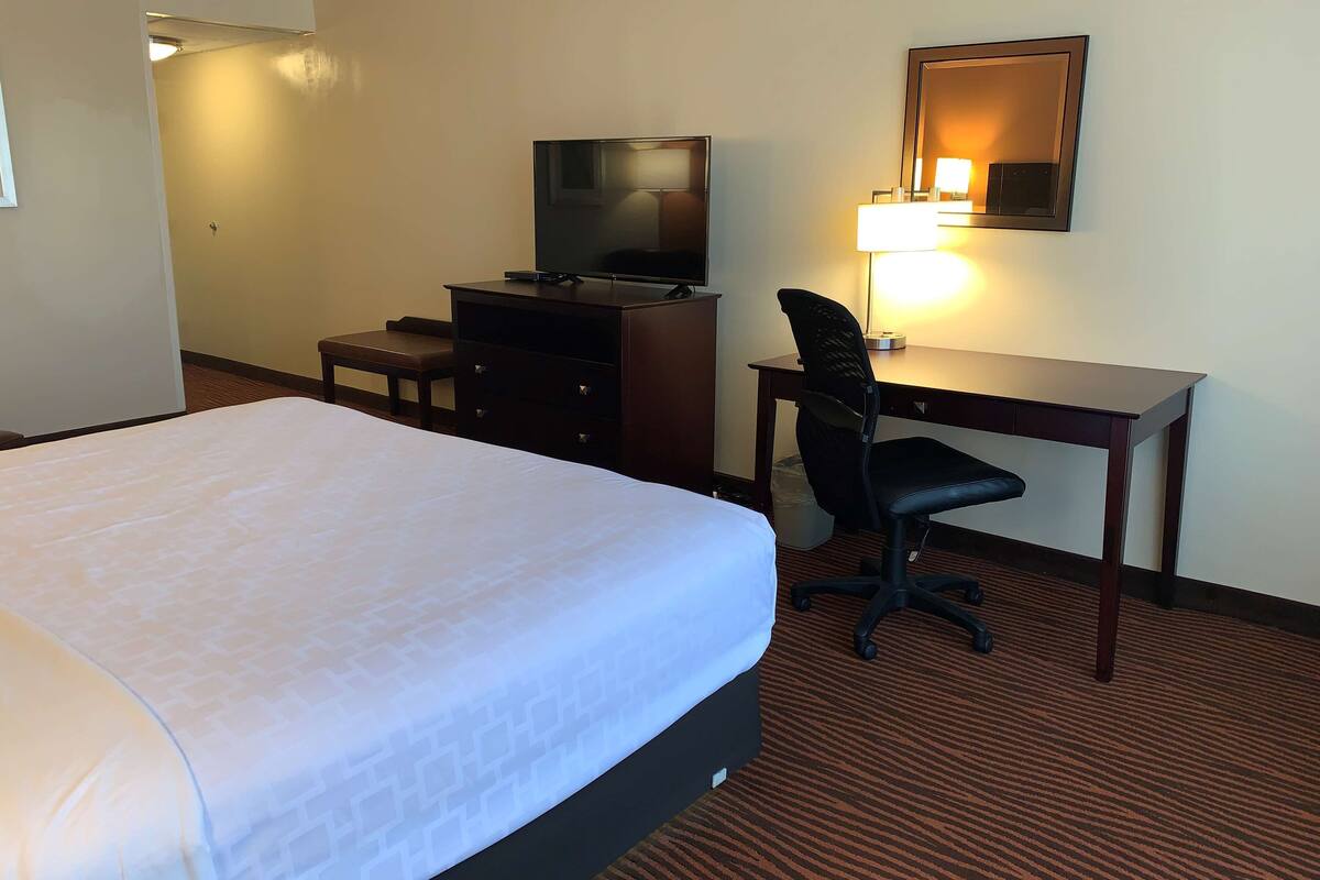A hotel room with a large bed, a desk with a chair, a television, and a lamp.