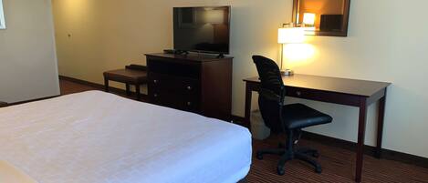 Una habitación de hotel con una cama grande, un escritorio con una silla, un televisor y una lámpara.