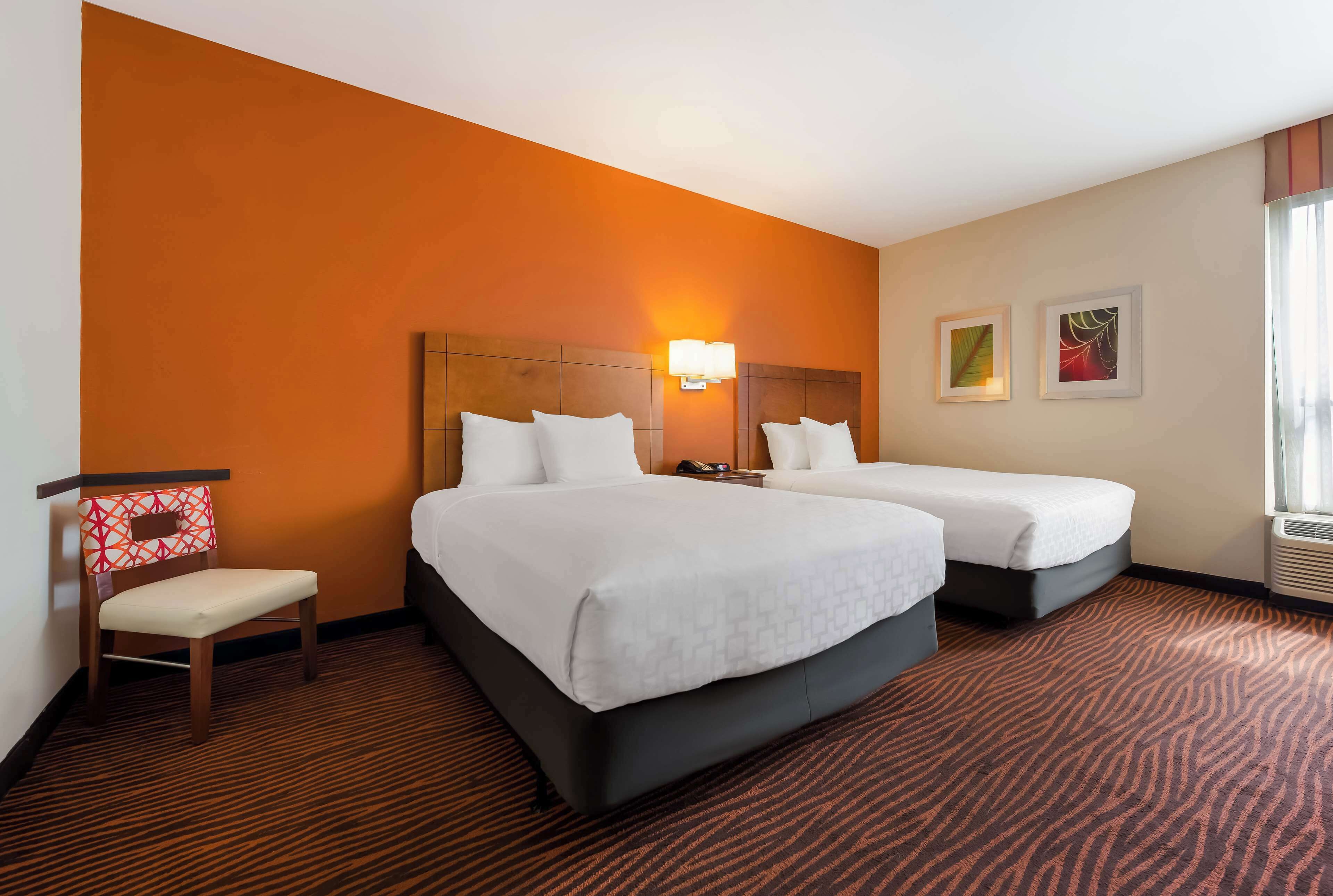 Habitación de hotel con dos camas, una silla y una mesita de noche.