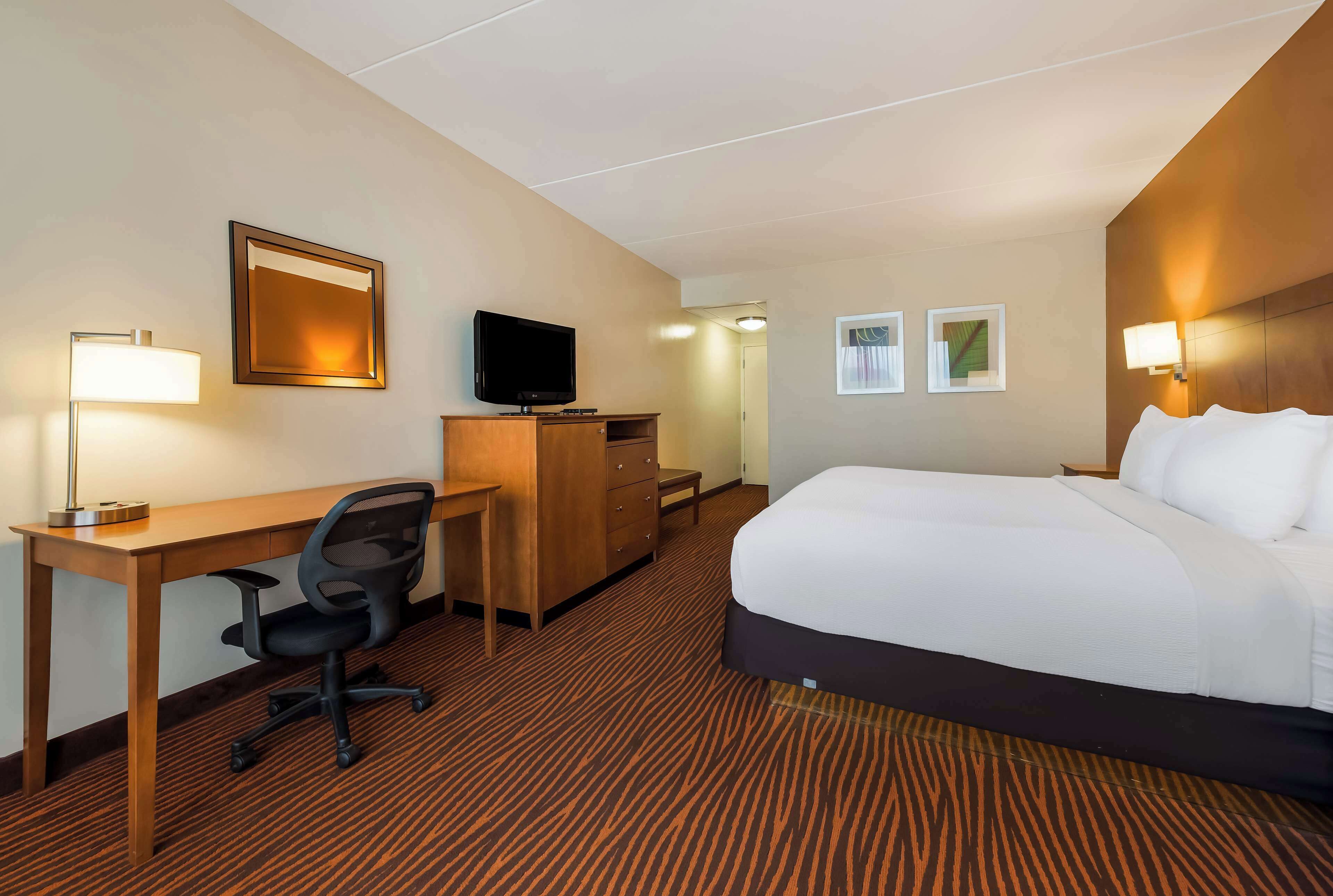 A hotel room with a bed, desk, chair, television, and wall-mounted lamps.